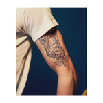 Ein mystisches Tattoo mit einer Frau mit Geweihen, umgeben von einem Totenschädel, Pilzen und einem Schmetterling. Der Halbmond oben fügt einen Hauch von Magie und Geheimnis hinzu. Dieses Design symbolisiert Transformation, das Gleichgewicht zwischen Leben und Tod und die Schönheit der Naturzyklen.