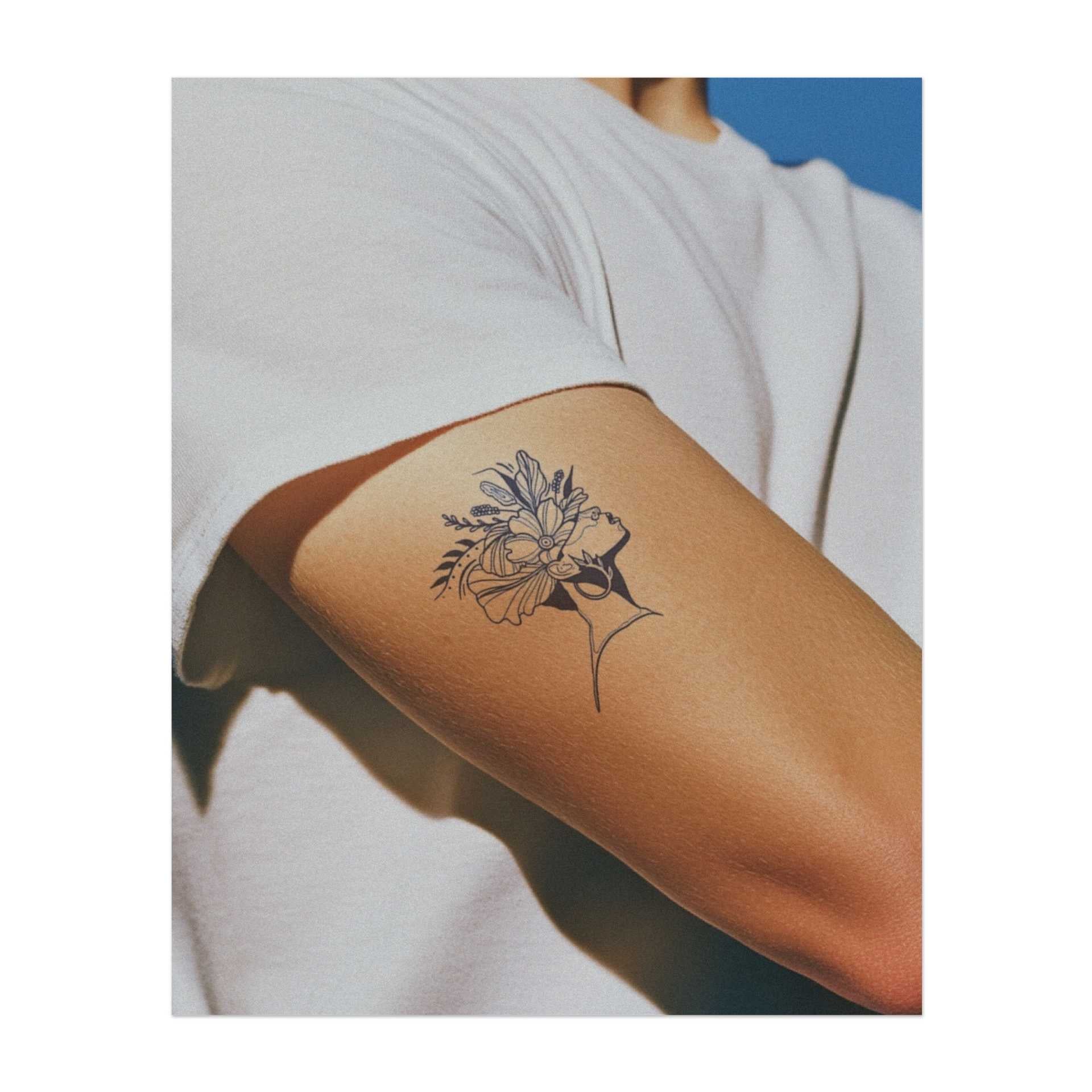 Ein zartes Profil einer Frau mit einer Krone aus lebendigen Blumen und Blättern. Dieses Tattoo symbolisiert Schönheit, Natur und innere Stärke. Perfekt für diejenigen, die Anmut, Wachstum und die Kraft der natürlichen Schönheit schätzen.